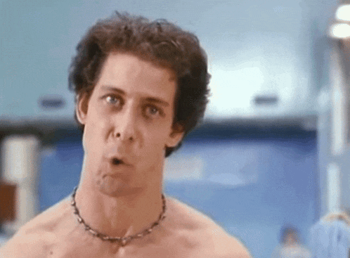 a shirtless man wearing a barbed wire necklace looks surprised