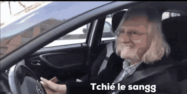 a man with long blonde hair is driving a car with the words tchie le sangg on the screen