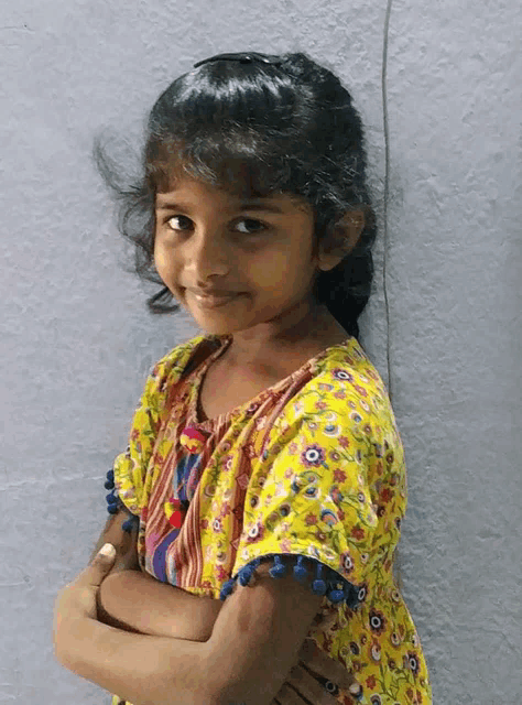 a little girl with her arms crossed is wearing a yellow shirt