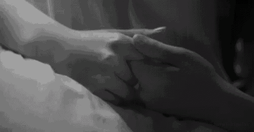 a black and white photo of a man and woman holding hands on a bed .