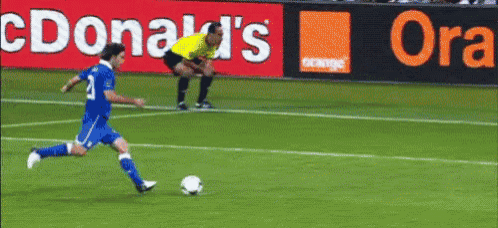 a soccer player is kicking a soccer ball on a field with a mcdonald 's and orange ad in the background