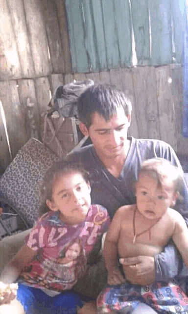 a man is holding two children one of whom is wearing a shirt that says " feliz "