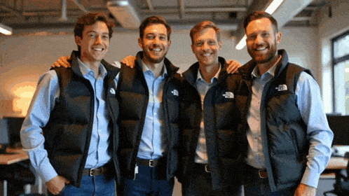 four men wearing vests with the north face on them