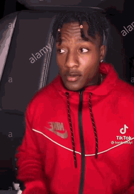 a young man in a red nike hoodie is sitting in a car and pointing at the camera .