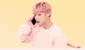 a young man with pink hair is talking on a cell phone while wearing a pink sweater .