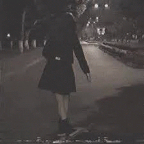 a black and white photo of a girl walking down a street at night .