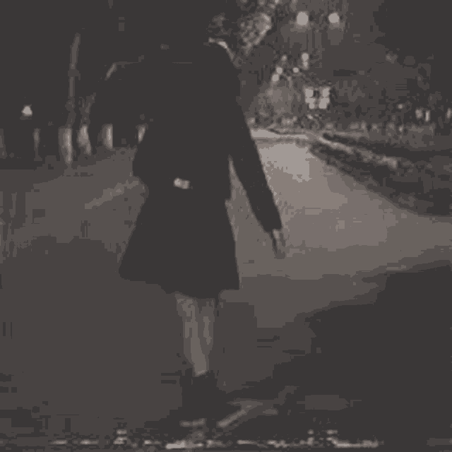 a black and white photo of a girl walking down a street at night .