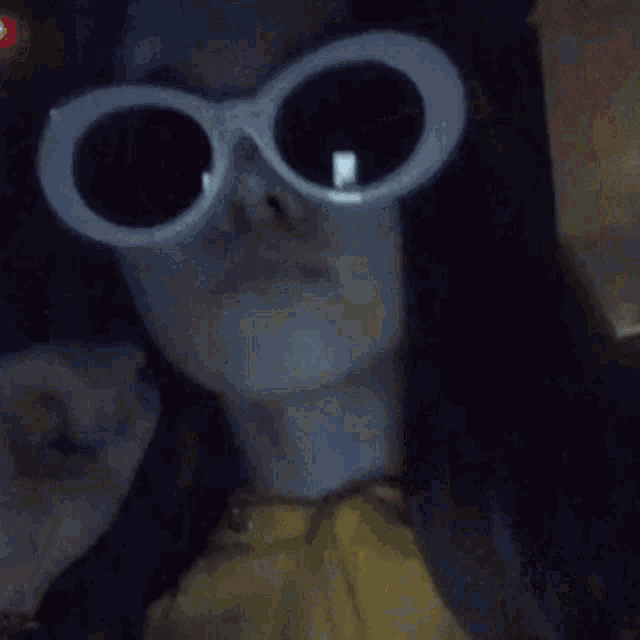 a woman wearing a yellow shirt and white sunglasses looks at the camera .