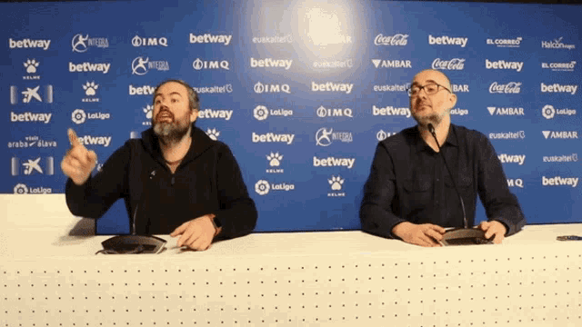 two men sitting at a desk in front of a wall that says ' betway '