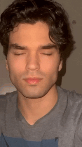 a young man with his eyes closed is wearing a gray shirt .