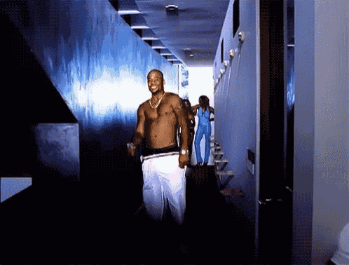 a man without a shirt is walking down a hallway with other men