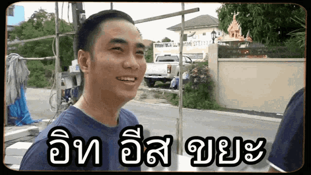 a man in a blue shirt is smiling in front of a fence and a truck