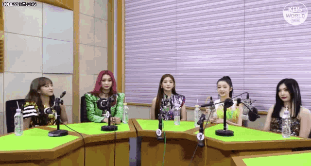 a group of women are sitting at a table in front of microphones in a radio studio .