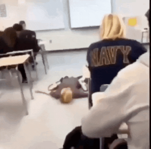 a woman in a navy shirt is sitting in a classroom with other students .