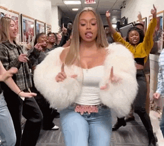 a woman wearing a white fur coat is dancing in a hallway with a group of people .
