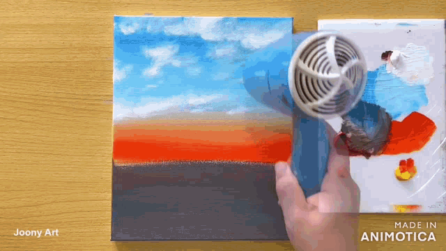 a person is using a hair dryer to dry a painting of a sunset