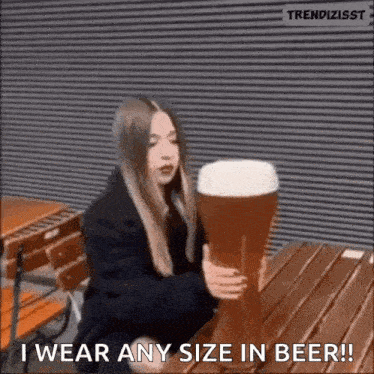 a woman is sitting at a table holding a very large beer glass .