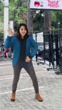 a woman in a blue jacket is waving in front of a sign that says magic pentol