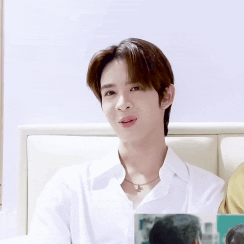 a young man wearing a white shirt and a necklace is making a funny face