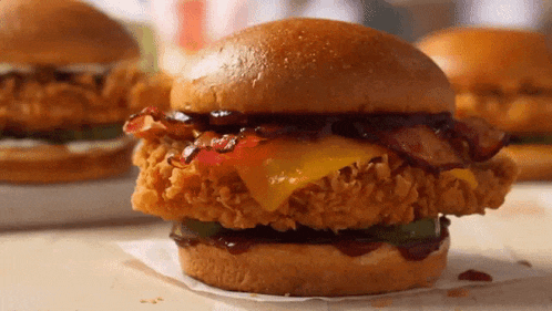 a fried chicken sandwich with cheese bacon and pickles on a bun