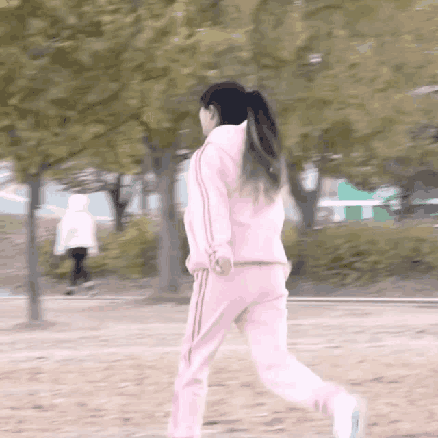a woman in a pink hoodie and pink sweatpants is running in a park