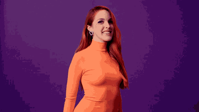 a woman with red hair is wearing a bright orange turtleneck and heart shaped earrings