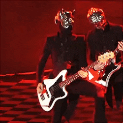 two men in masks are playing guitars on a stage in front of a red background .