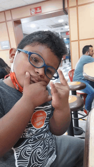 a boy wearing glasses and a california paradise shirt giving the middle finger