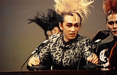 a man with a mohawk stands in front of a microphone with a watermark that says " marysue-complex "