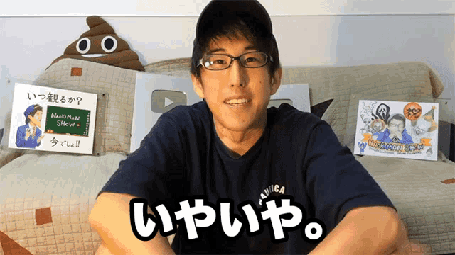 a man wearing glasses sits on a couch in front of a sign that says " nakamura shin "