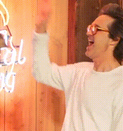 a man wearing glasses and a white shirt stands in front of a neon sign that says ' cool nuts '