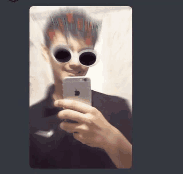 a man is taking a selfie with his phone while wearing sunglasses .
