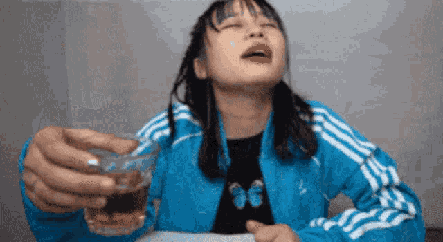 a woman in a blue jacket is holding a shot glass of alcohol .