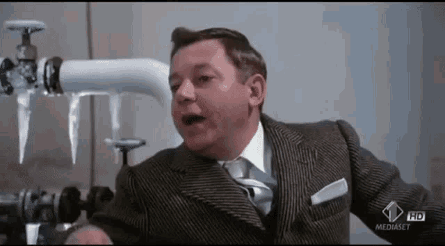 a man in a suit and tie is sitting in front of a pipe with icicles coming out of it
