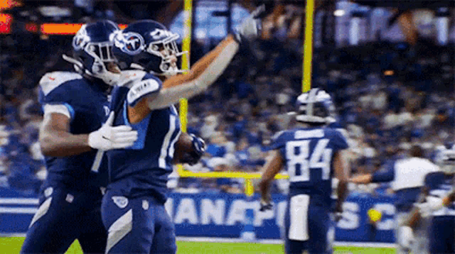 two football players are hugging each other on a field . one of the players has the number 84 on his jersey .