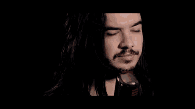 a man with long black hair and a beard is holding a microphone in his hand .