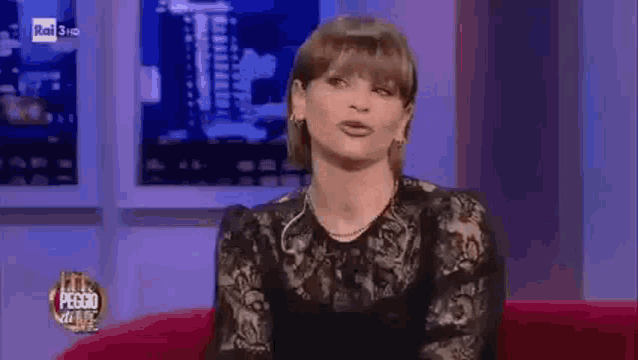 a woman is sitting on a red couch in front of a television and making a funny face .