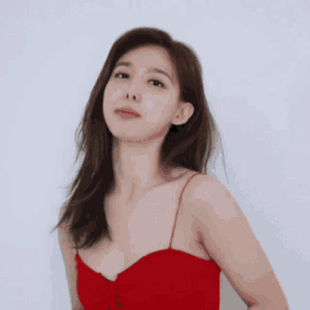 a woman in a red tank top is standing in front of a white wall and looking at the camera .
