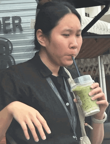 a woman drinking from a plastic cup with a straw and a lanyard that says ' starbucks '
