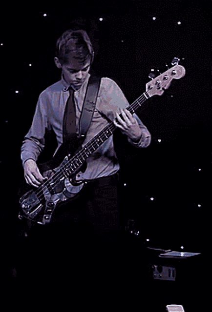 a man in a tie is playing a bass guitar on a stage