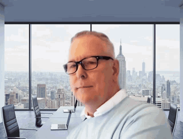 a man wearing glasses stands in front of a large window overlooking the city