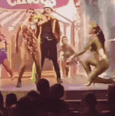 a group of people are dancing on a stage in front of a crowd at a circus .