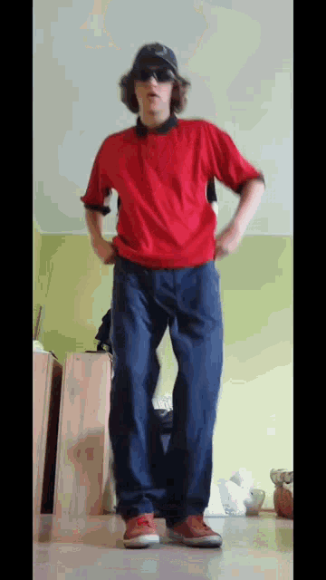 a man wearing sunglasses and a red shirt is standing with his hands in his pockets