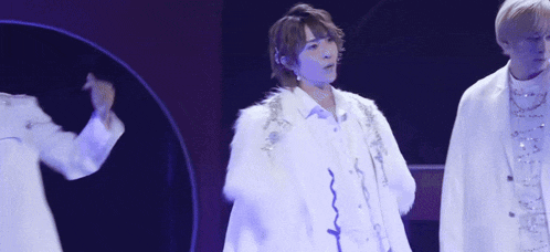 a man in a white fur coat is standing on a stage with other people