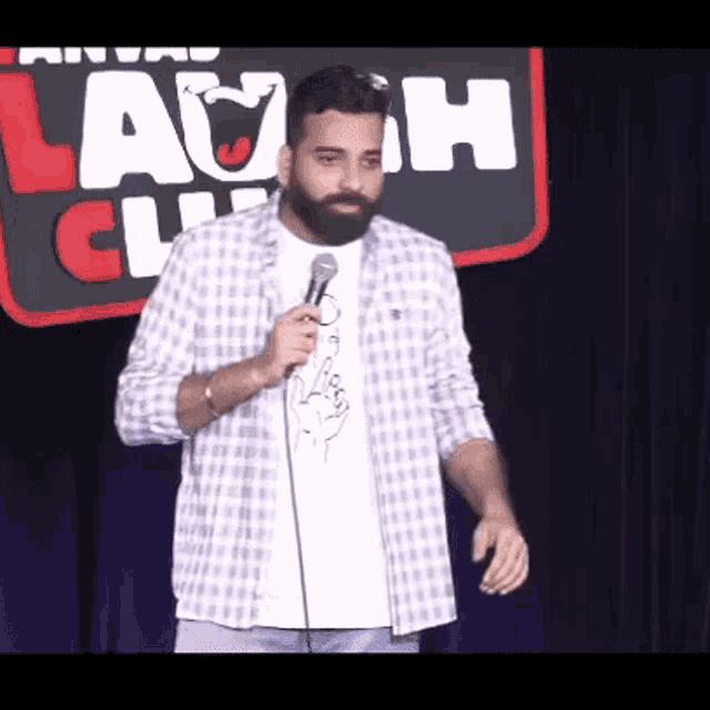a man with a beard is holding a microphone on stage in front of a sign that says laugh club .