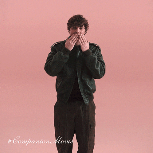 a man in a green jacket is standing in front of a pink background with # companion movie written on it
