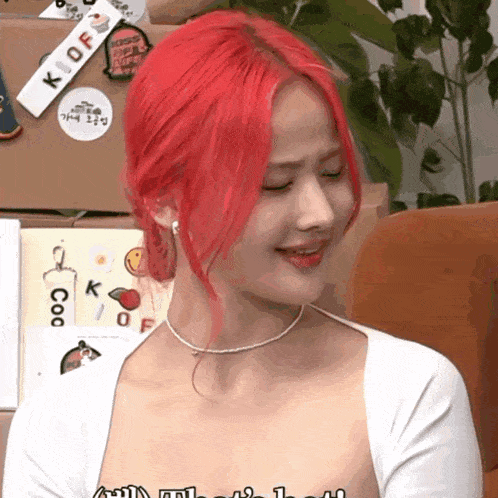 a woman with red hair is wearing a white top and a necklace with the letter k on it