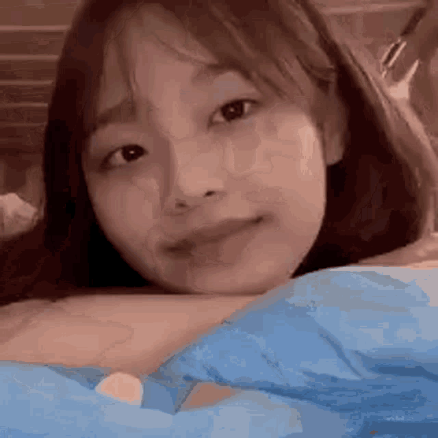 a young girl is laying on a bed with a blue blanket and looking at the camera .