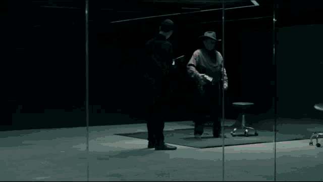 a man in a cowboy hat stands next to another man in a dark room