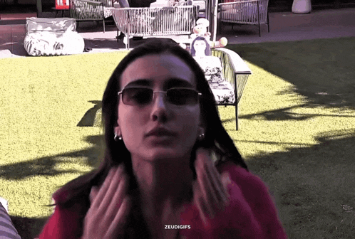 a woman wearing sunglasses and earrings is sitting on a lawn .